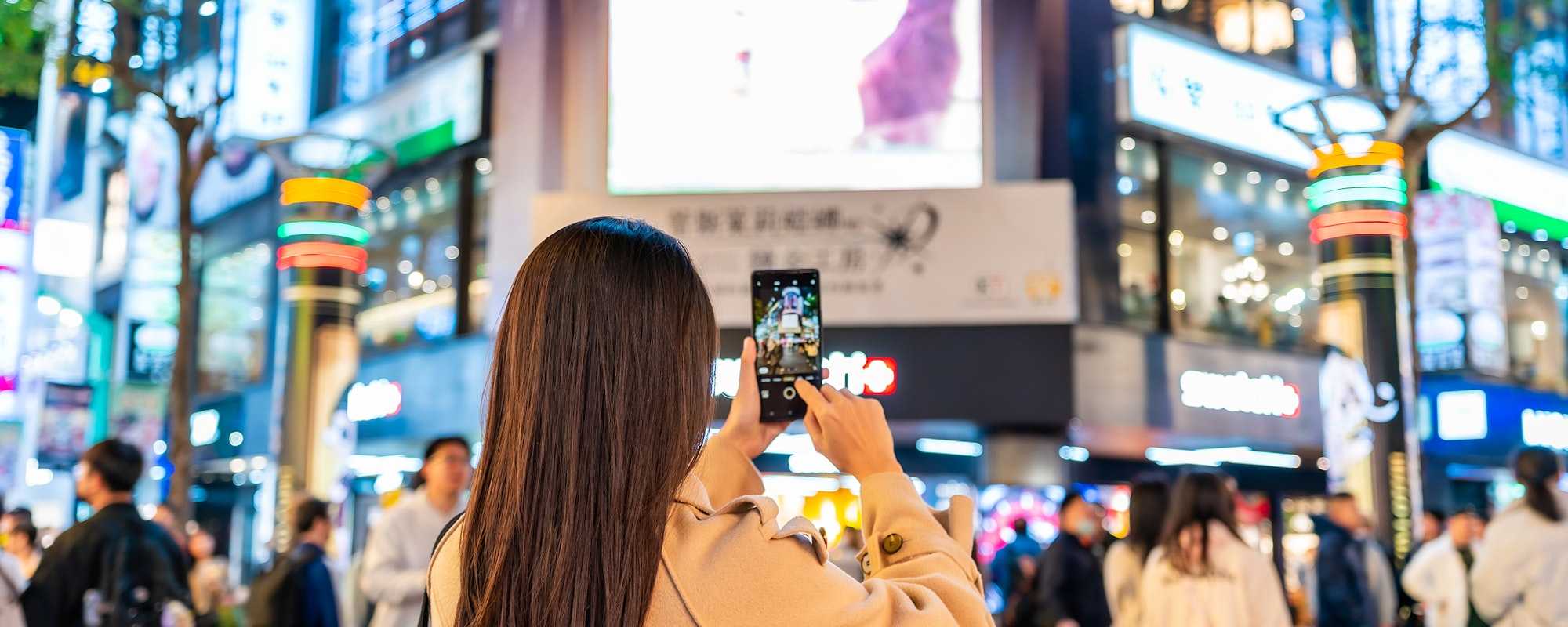 Busy city centre with woman taking photo of advertising screens