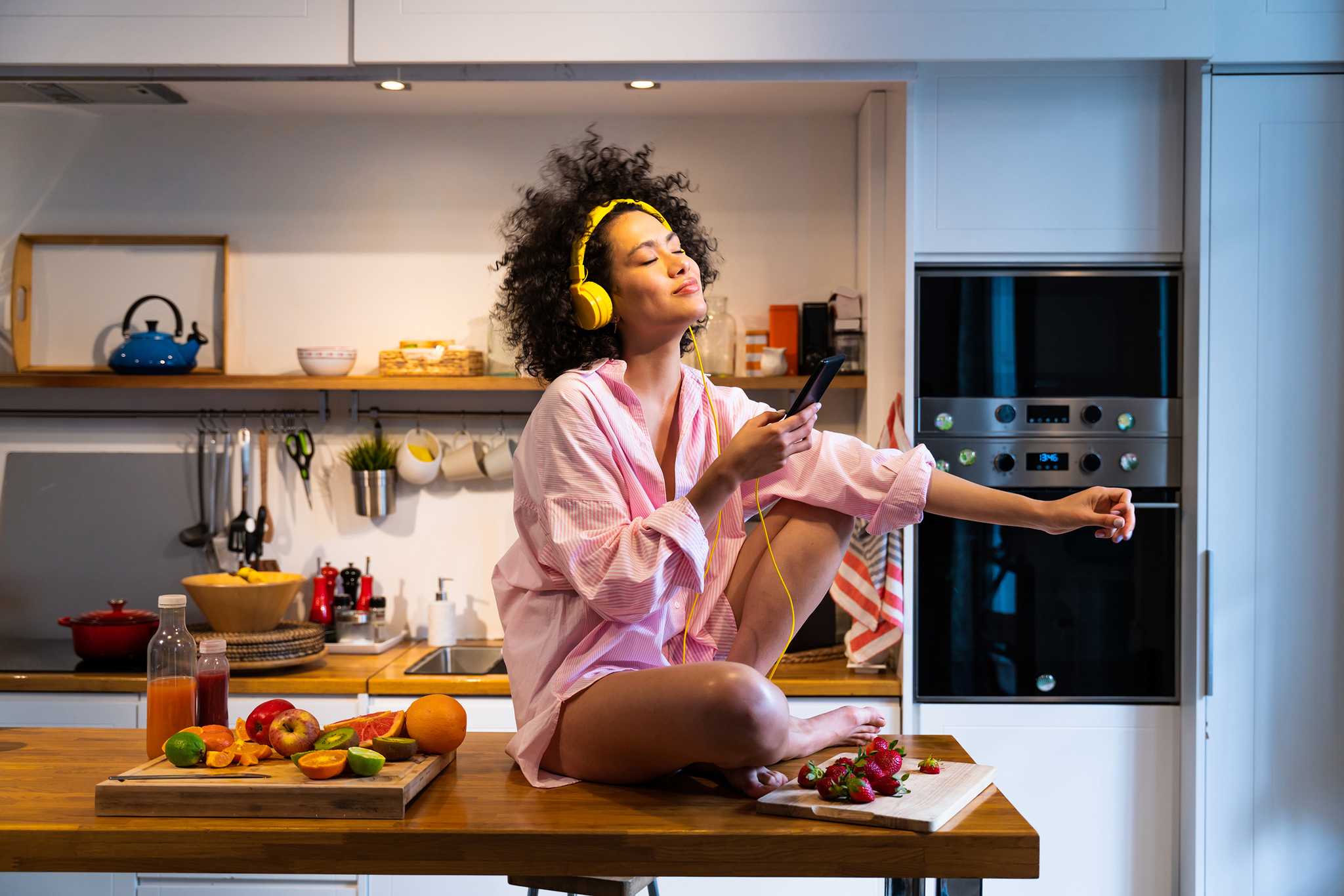 Woman on kitchen table listening to music on headphones