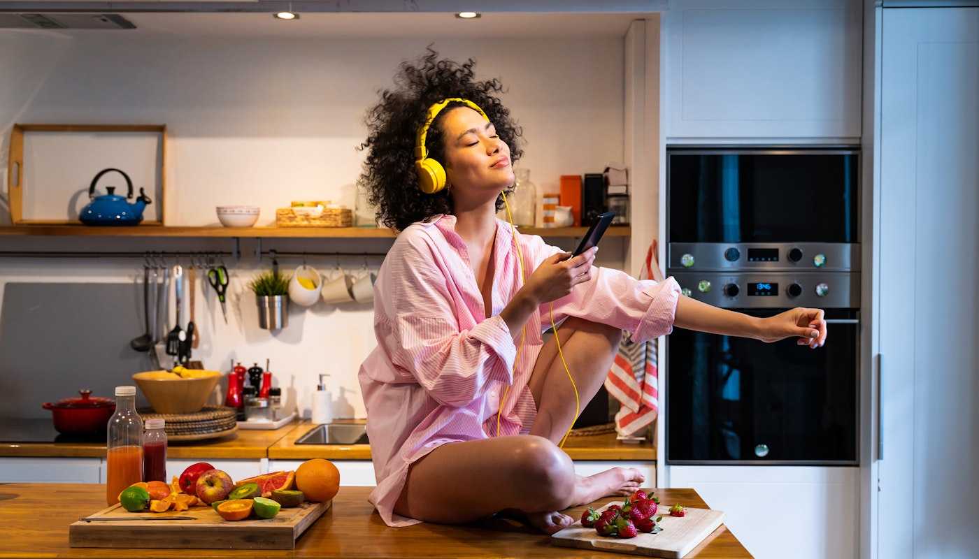 Woman on kitchen table listening to music on headphones