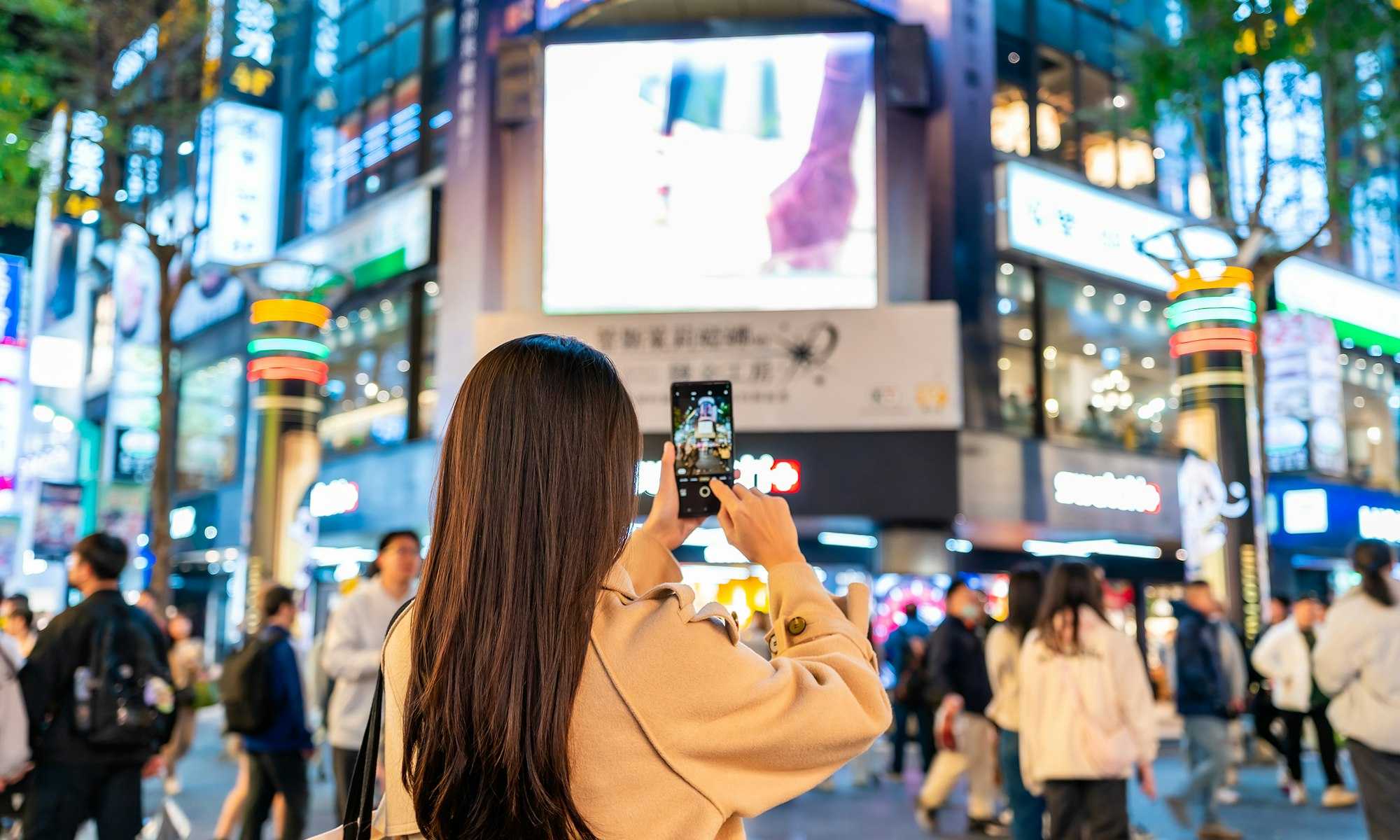 Busy city centre with woman taking photo of advertising screens