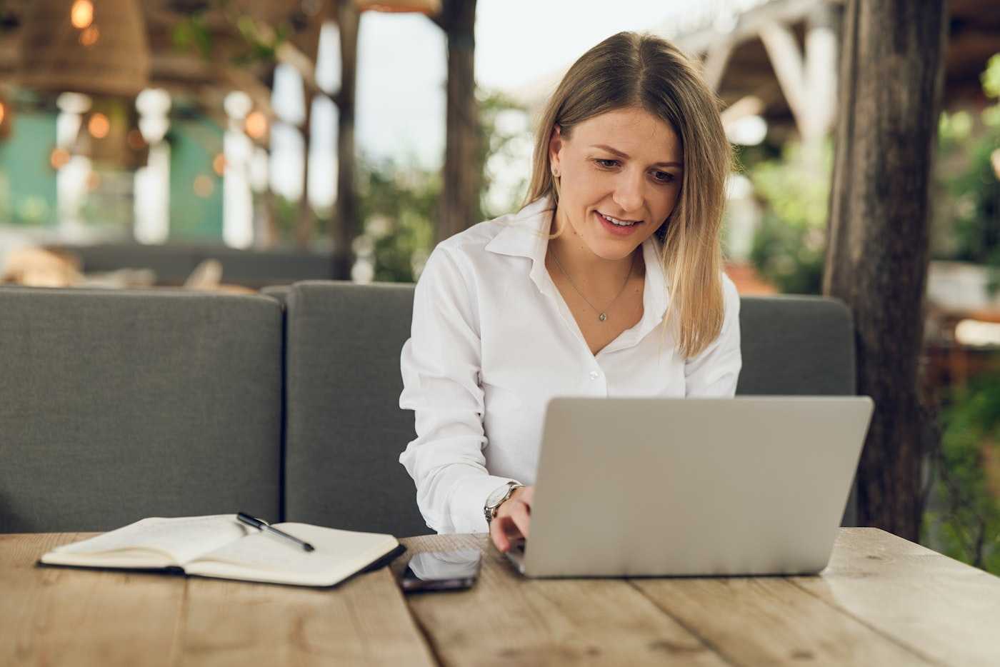 Female copywriter typing on a laptop while sitting in a cozy outdoor cafe | Belong Creative